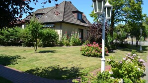 A house with a sloped roof, surrounded by a well-maintained garden with various flowering plants and a lawn. - N 40 GH 4-room Terr. (BC.n5) - Stranddomicil Steiner - Guesthouses (Büsum)