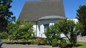 A house with a tiled roof, a circular front porch, and a garden with various plants and flowers. - N 40 GH 4-room Terr. (BC.n5) - Stranddomicil Steiner - Guesthouses (Büsum)