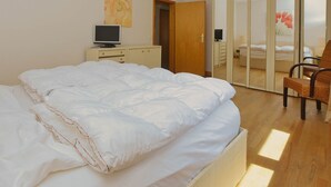 A bedroom with a large bed, a TV on a bedside table, a wardrobe, and a chair. - N 40 GH 4-room Terr. (BC.n5) - Stranddomicil Steiner - Guesthouses (Büsum)