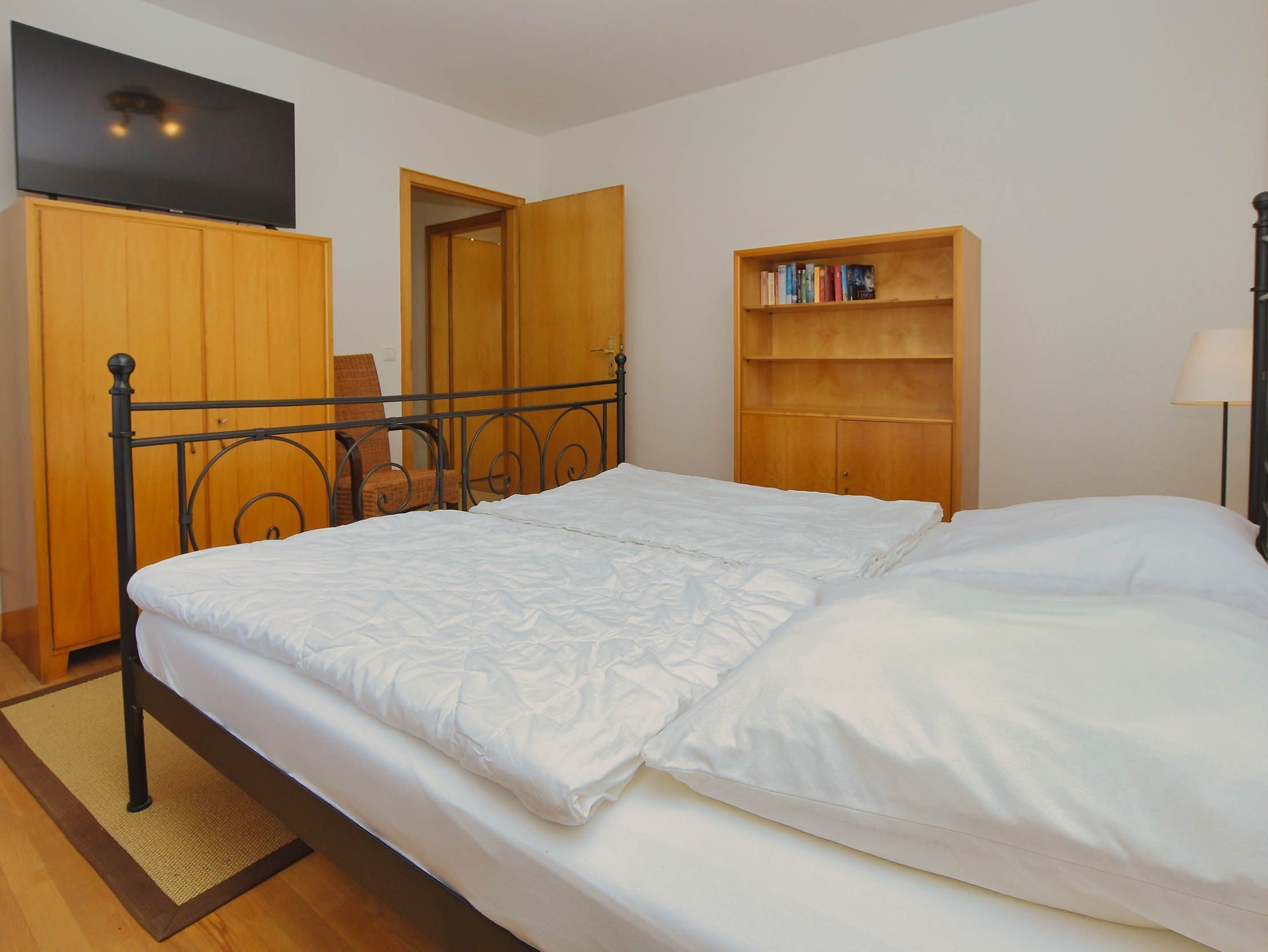 A bedroom with a bed, a wooden wardrobe, a bookshelf, and a chair.