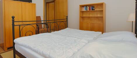 A bedroom with a bed, a wooden wardrobe, a bookshelf, and a chair.