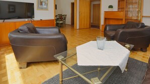 A living room with a TV, leather sofas, a glass coffee table, and a wooden cabinet. - N 40 GH 4-room Terr. (BC.n5) - Stranddomicil Steiner - Guesthouses (Büsum)