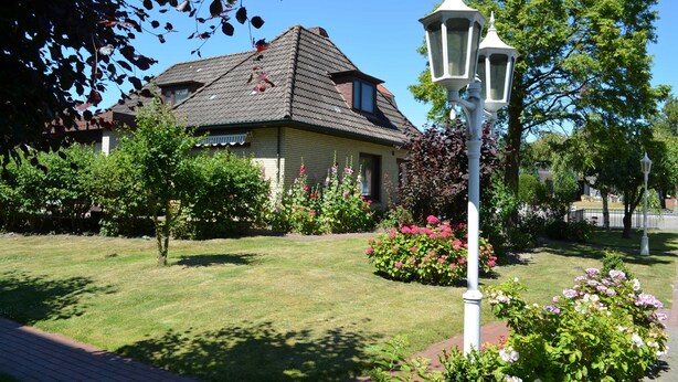 A house with a sloped roof, surrounded by a well-maintained garden with various plants and flowers.