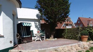 A patio area with a stone border, a table with a striped umbrella, and a chair.