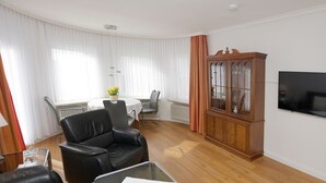 A living room with a black leather sofa, a glass coffee table, a wooden cabinet, and a television mounted on the wall.