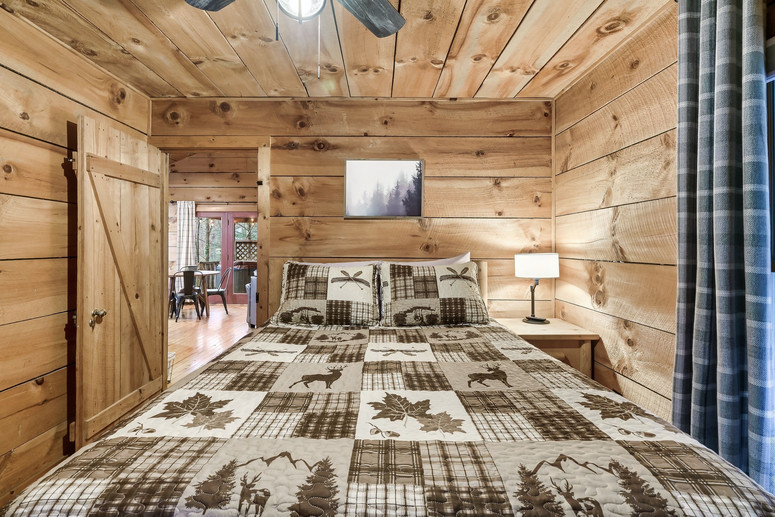 A wooden cabin bedroom with a bed, a nightstand, a lamp, and a painting on the wall.
