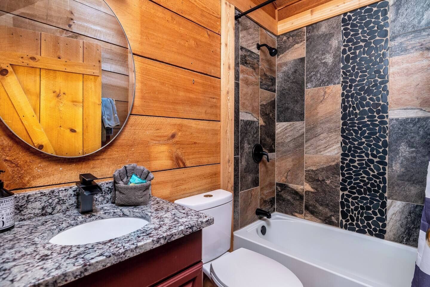 Un baño con paneles de madera, encimera de granito, inodoro blanco y bañera con azulejos de piedra.