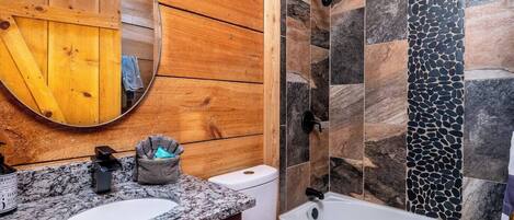Un baño con paneles de madera, encimera de granito, inodoro blanco y bañera con azulejos de piedra.