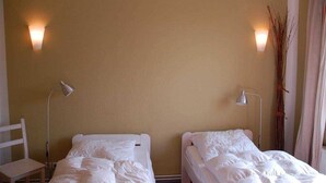 Quarto com duas camas, cada uma com roupa de cama branca e uma luminária ao lado.