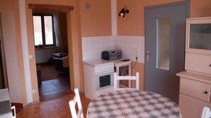 Cozinha compacta com micro-ondas, forno pequeno e pia. Há uma mesa de jantar com toalha quadriculada.
