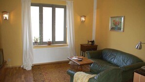 Uma sala de estar acolhedora com um sofá verde, uma mesa de centro de madeira e uma janela com cortinas brancas.