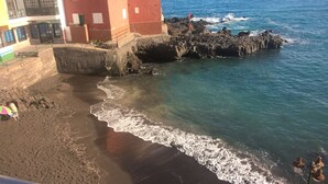 Une plage avec une digue rocheuse, une eau d’un bleu limpide et un bâtiment à la façade rouge.