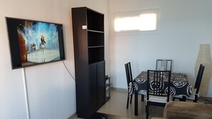 Un salon avec un téléviseur à écran plat fixé au mur, un meuble de rangement noir, une table à manger avec des chaises et un canapé.