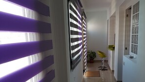 Un couloir avec un sol carrelé, une plante en pot et une chaise jaune.