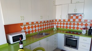 Une cuisine avec des meubles blancs, un four à micro-ondes, un évier et une cuisinière. On peut voir un saladier rempli de bananes et une bouteille de vin sur le comptoir.