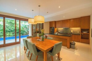 A modern kitchen with wooden cabinets, a central island, and pendant lighting. - Maca Villas SPA Umalas (Kerobokan)