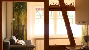 Ein gemütliches Zimmer mit einer Couch, einem Reh-Gemälde, einem Fenster mit Blick auf ein Haus und einer Holzleiter.