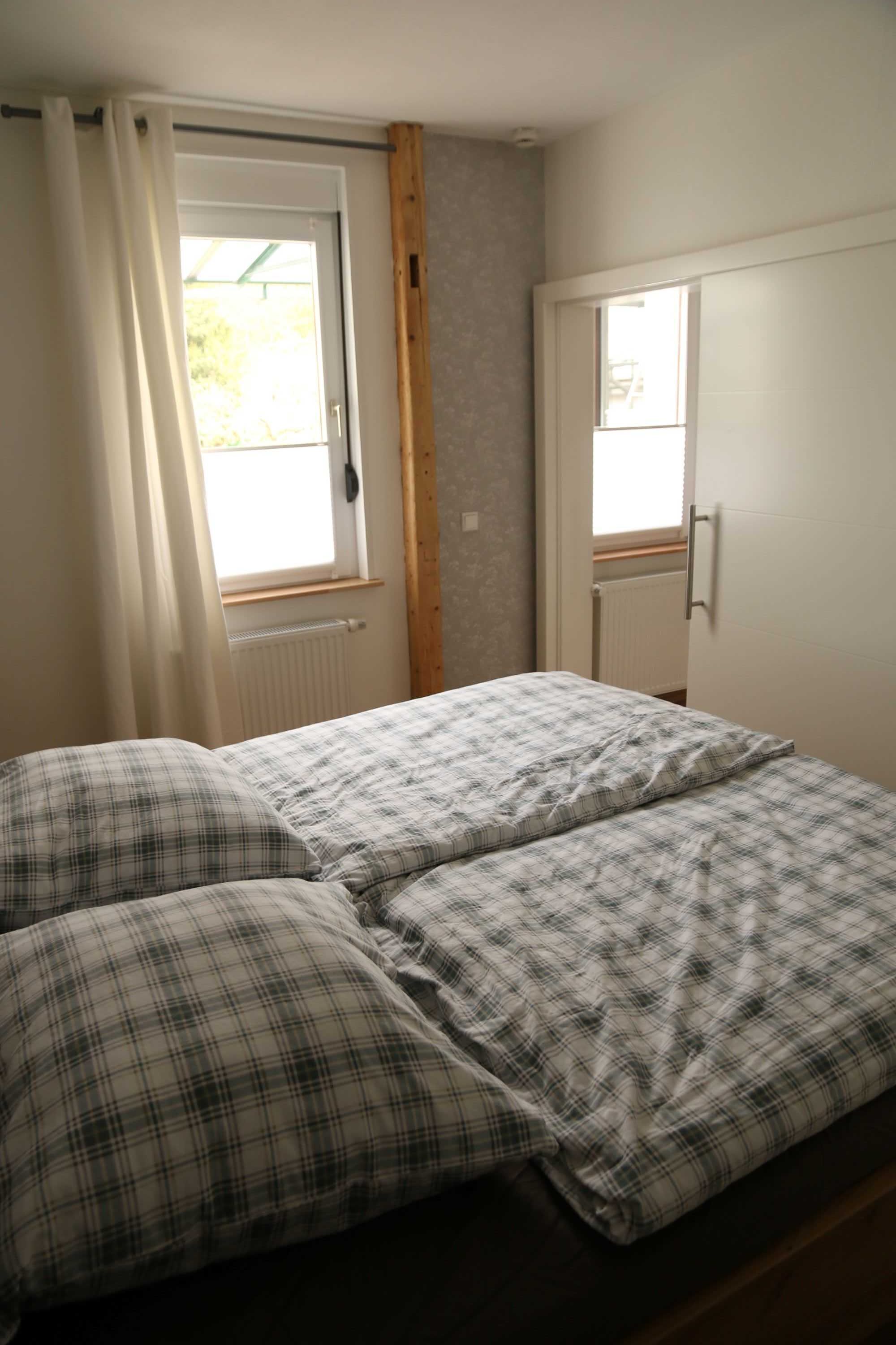 Ein Schlafzimmer mit einem Bett, zwei Kissen, einem Fenster mit Vorhängen und einer Heizung.