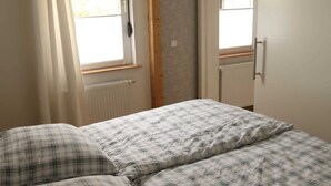 Ein Schlafzimmer mit einem Bett, zwei Kissen, einem Fenster mit Vorhängen und einer Heizung.