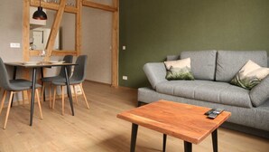 Ein Wohnzimmer mit grauem Sofa, einem Holztisch und einem Essbereich mit Tisch und Stühlen.