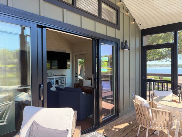 A modern living space with a sliding glass door leading to a deck, a sofa, and a dining table with chairs.