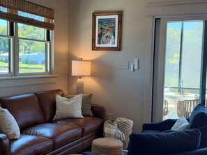 A living room with a brown leather sofa, a blue armchair, a lamp, and a framed painting on the wall.