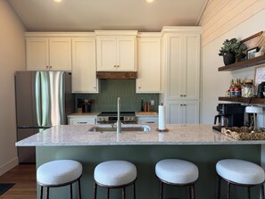 A kitchen with white cabinets, a stainless steel refrigerator, a marble countertop, and a wooden island with bar stools.