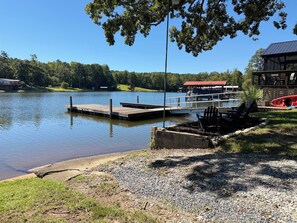 A lakeside dock with a boat, a covered seating area, and a building with a red roof.