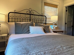 A neatly made bed with a metal headboard, two bedside lamps, and a window with a view.