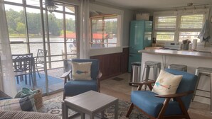 Una habitación acogedora con vistas a un lago, que incluye dos sillones azules, una mesita y una zona de cocina.