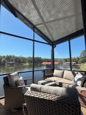 A sunlit room with a view of a lake, featuring a sofa set and wicker furniture.