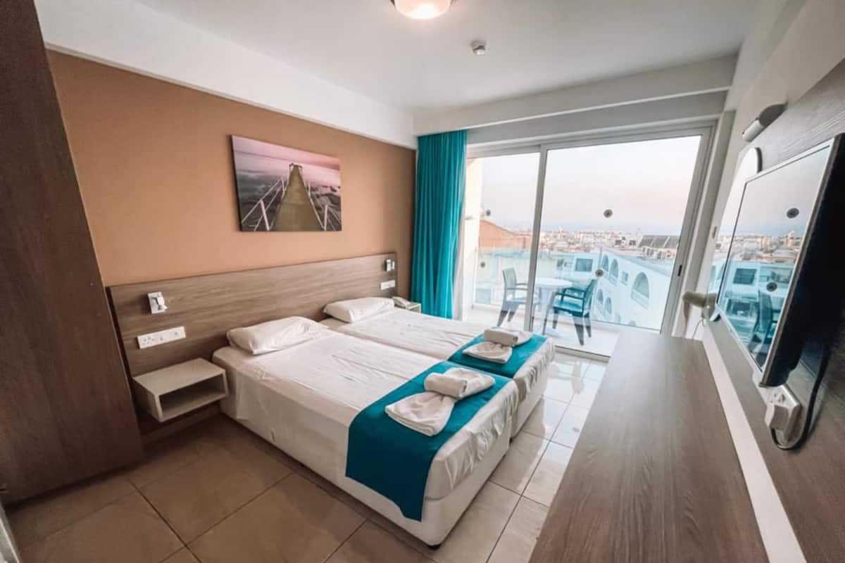 Une chambre d’hôtel avec deux lits, un bureau, une télévision et un balcon donnant sur la ville.