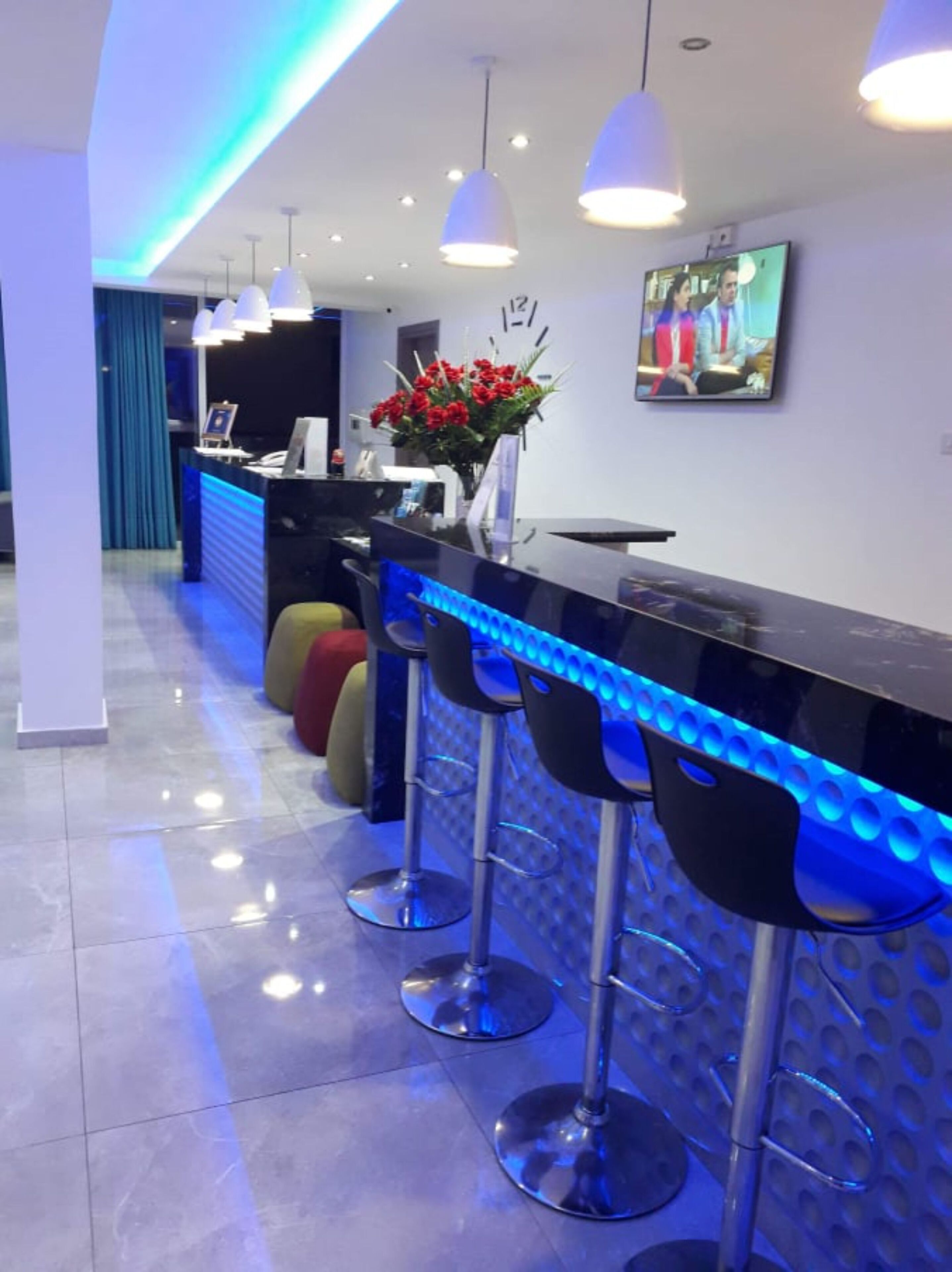 A modern bar area with a black countertop, blue LED lighting, and three black bar stools.