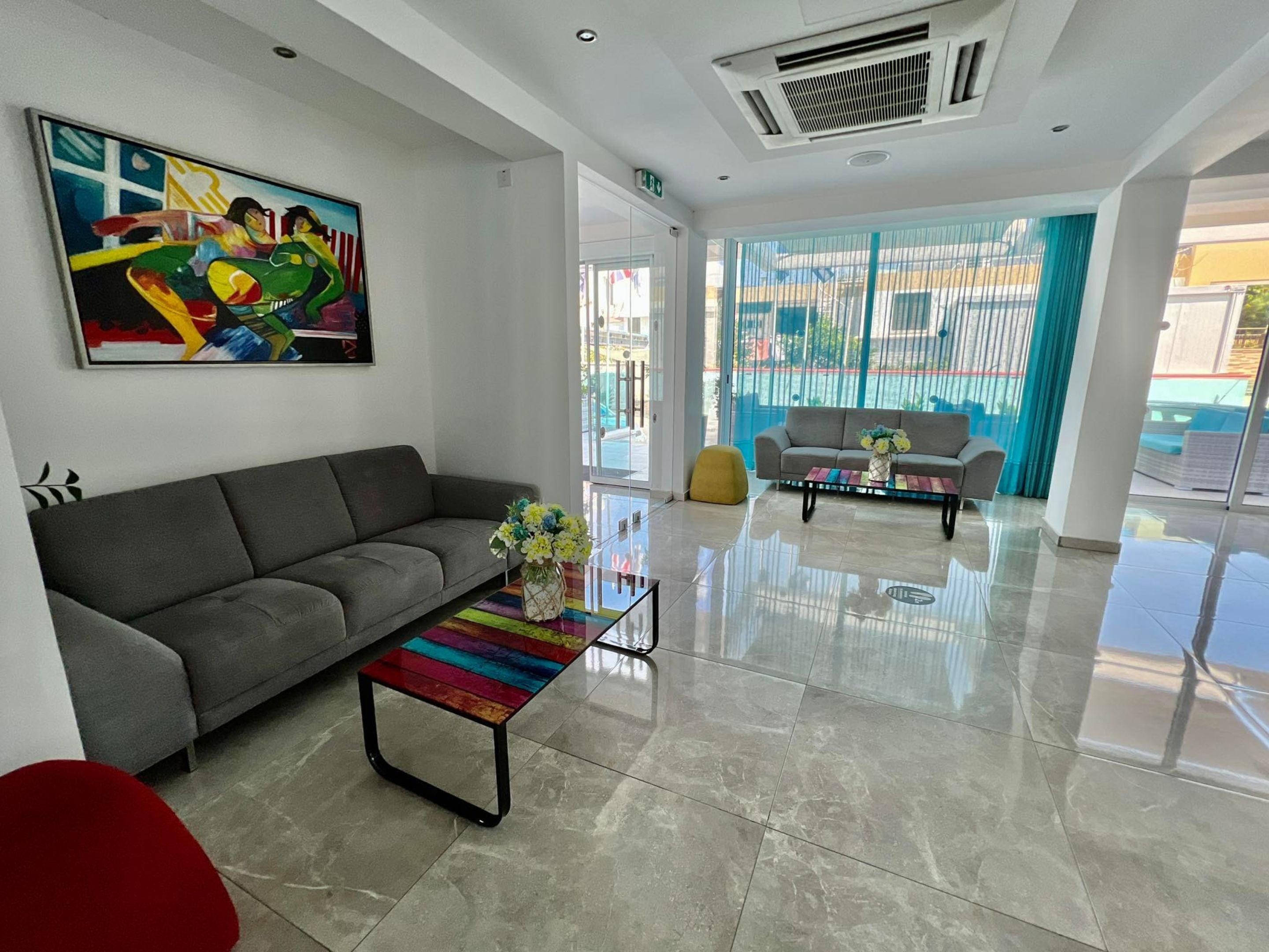 A modern hotel lobby with a grey sofa, a colorful coffee table, and a large abstract painting.