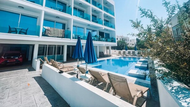 Un hôtel à plusieurs étages doté d’une piscine, d’un espace extérieur aménagé et surplombant un ciel d’un bleu limpide.