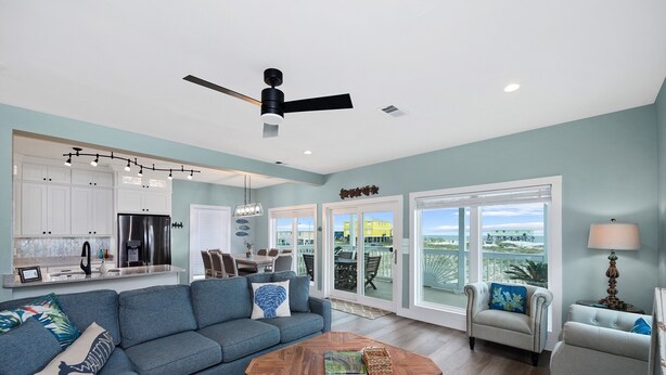 A spacious living room with a blue sofa, a coffee table, and a dining area with a kitchen in the background. - Dog Friendly Private Beach House in Beautiful Fort Morgan, Alabama!  (Gulf Shores)