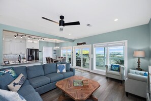 A spacious living room with a blue sofa, a coffee table, and a dining area with a kitchen in the background. - Dog Friendly Private Beach House in Beautiful Fort Morgan, Alabama!  (Gulf Shores)
