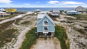 A coastal house with a balcony, surrounded by a sandy beach and other buildings. - Dog Friendly Private Beach House in Beautiful Fort Morgan, Alabama!  (Gulf Shores)