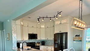 A modern kitchen with white cabinetry, a central island, and a dining area with a large table and chairs. - Dog Friendly Private Beach House in Beautiful Fort Morgan, Alabama!  (Gulf Shores)