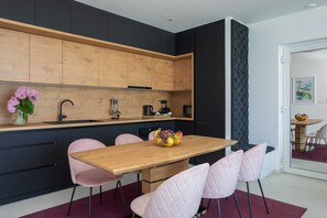 A modern kitchen with wooden cabinets, a black countertop, and a wooden dining table with pink chairs.