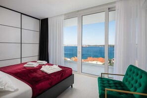 A modern hotel room with a bed, a green chair, and a large window offering a sea view.