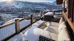 Zona de estar al aire libre cubierta de nieve, con vista a un pueblo y montañas.