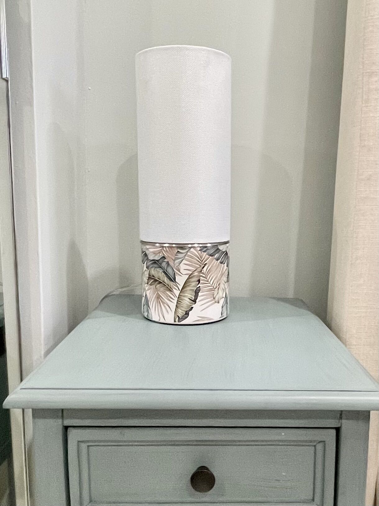 Uma mesa de cabeceira com abajur, com padrão de folhas.