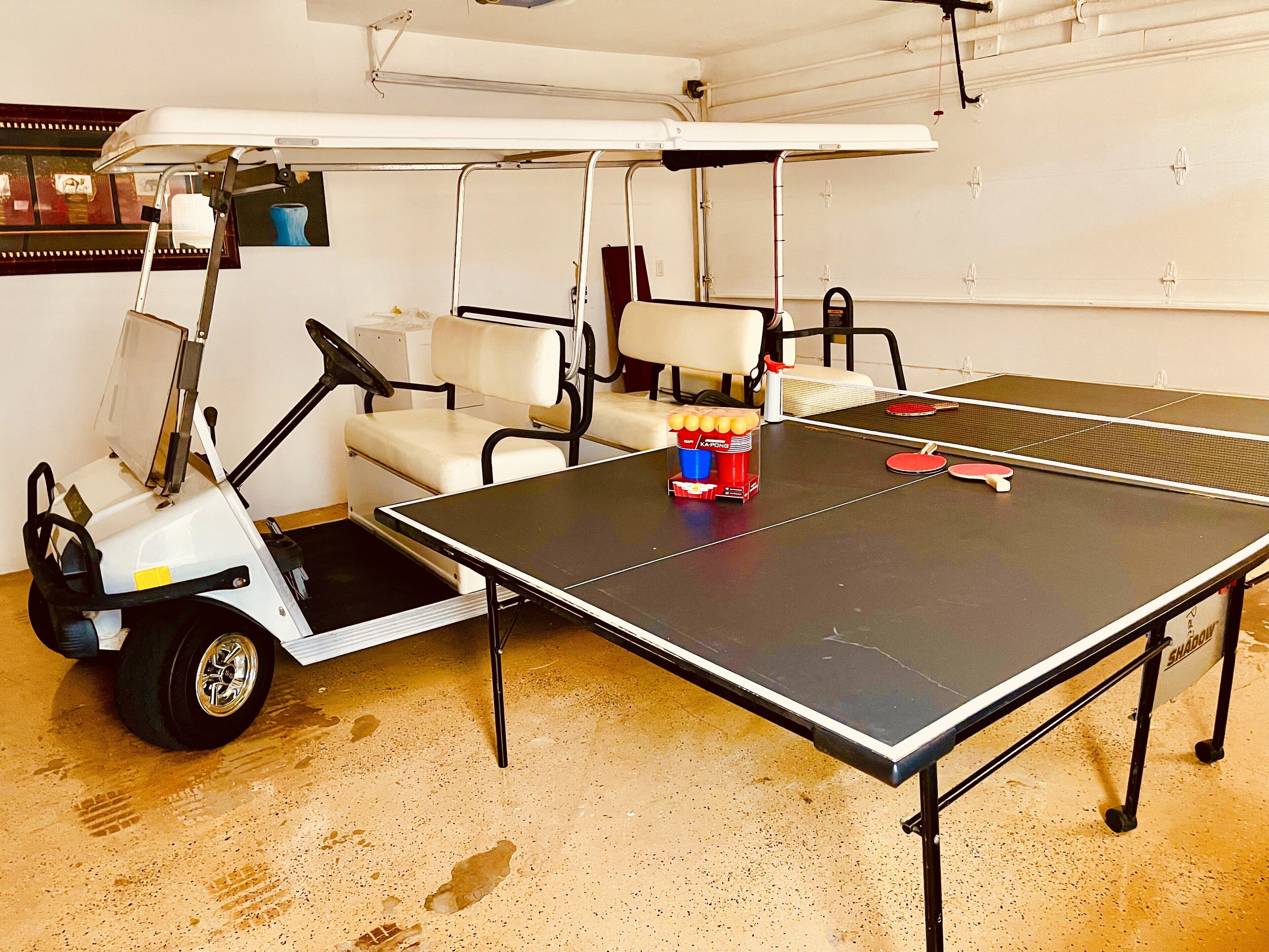 A ping pong table with paddles and balls, a golf cart, and a white chair.