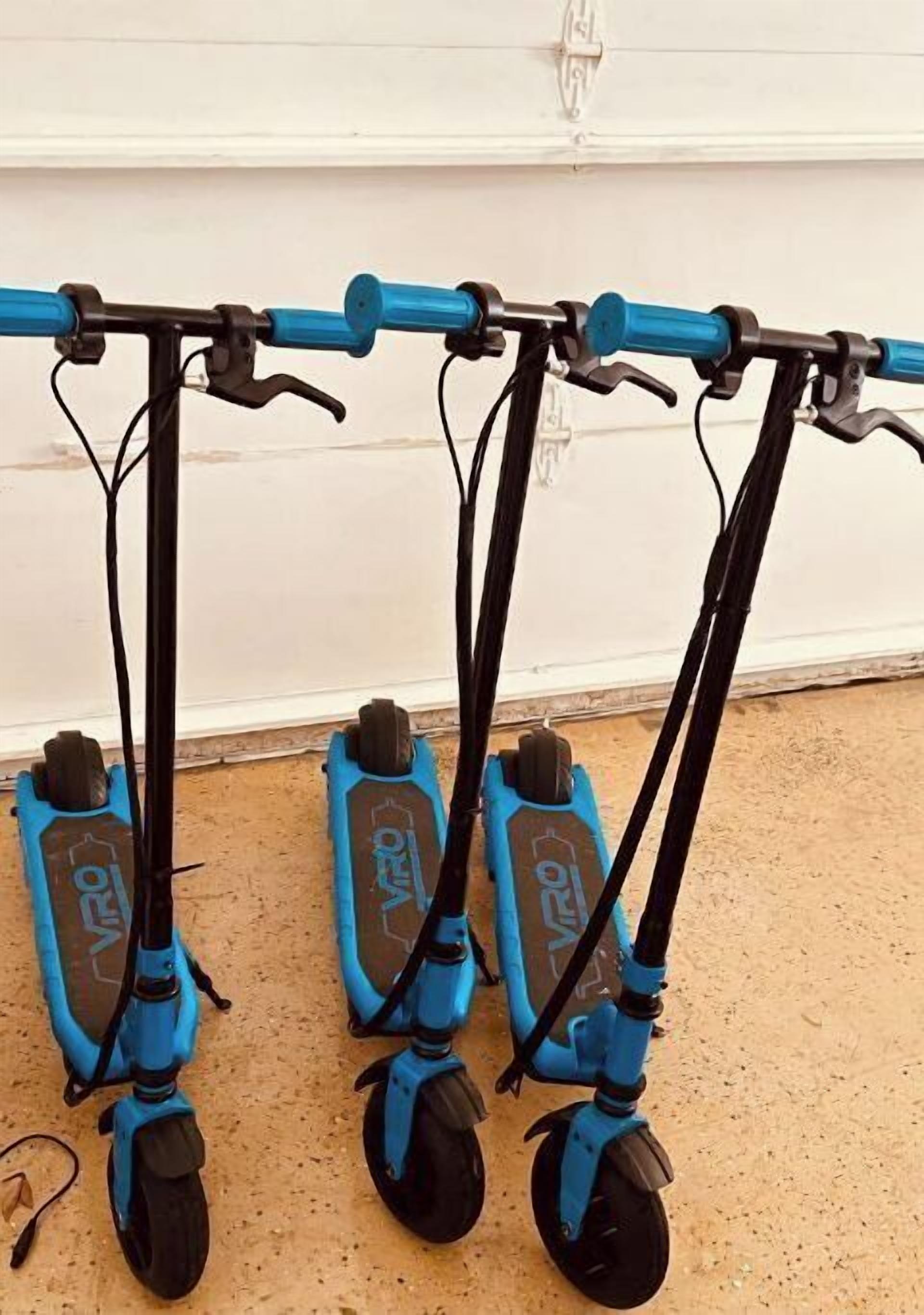 Three blue electric scooters parked against a wall.