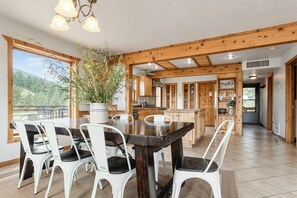 Un vaste espace dédié à la salle à manger, avec une table en bois foncé et des chaises blanches, une plante en pot et une vue sur l’extérieur.