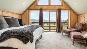 Ein Schlafzimmer mit einem großen Bett, einem Sessel und Blick ins Freie.