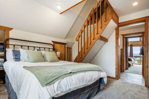 Une chambre avec un grand lit, un escalier en bois et une vue sur l’extérieur.