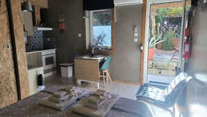 A compact kitchen with a sink, stove, and a small trash bin. There is a dining area with a table and chairs, and a window with a view of the garden. - Ruby Charm Houses 11 116353/AL (Porto)