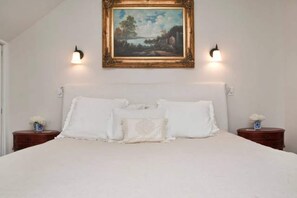 A bedroom with a large bed, two bedside tables, a framed painting above the bed, and wall-mounted lights. - Central Castro 2BR w/ Private Deck, Garden and Laundry- NO STAIRS! (San Francisco)